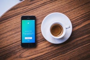 Twitter Marketing for Travel Enthusiasts: How to Boost Twitter Impressions from Scratch? phone with w twitter open and coffee